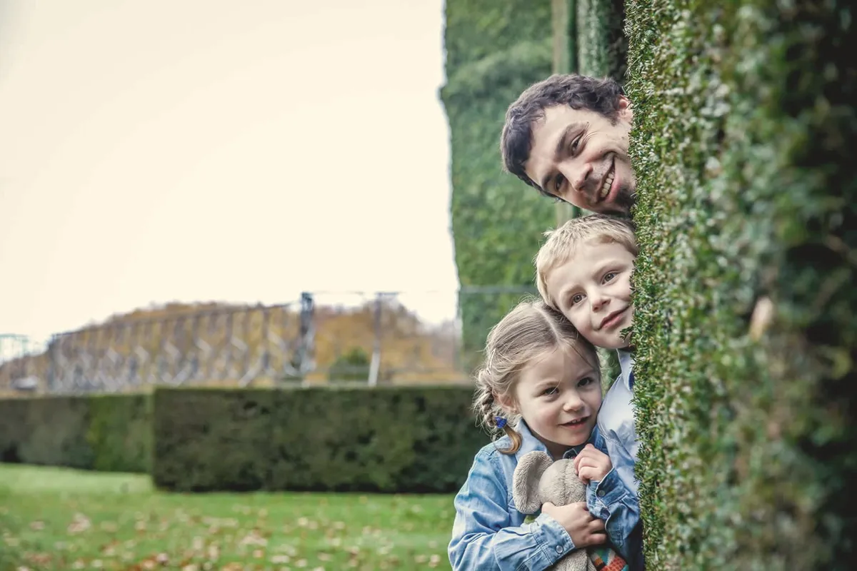 Trois visages qui se cachent derrière une haie.