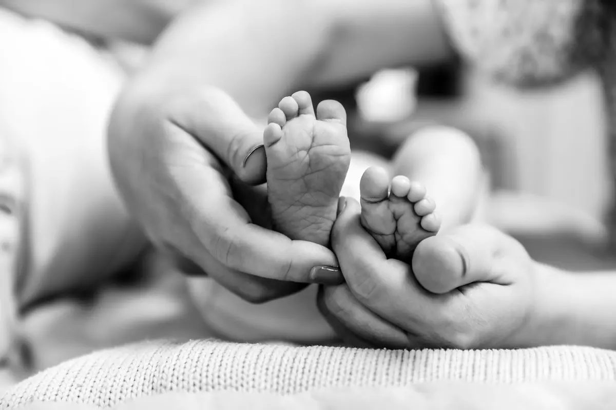 En noir et blanc, les pieds d’un bébé dans les mains de ses parents.