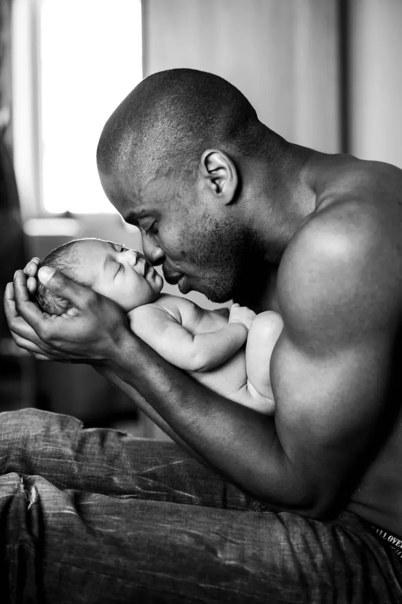 En noir et blanc, un papa embrasse son nouveau-né.