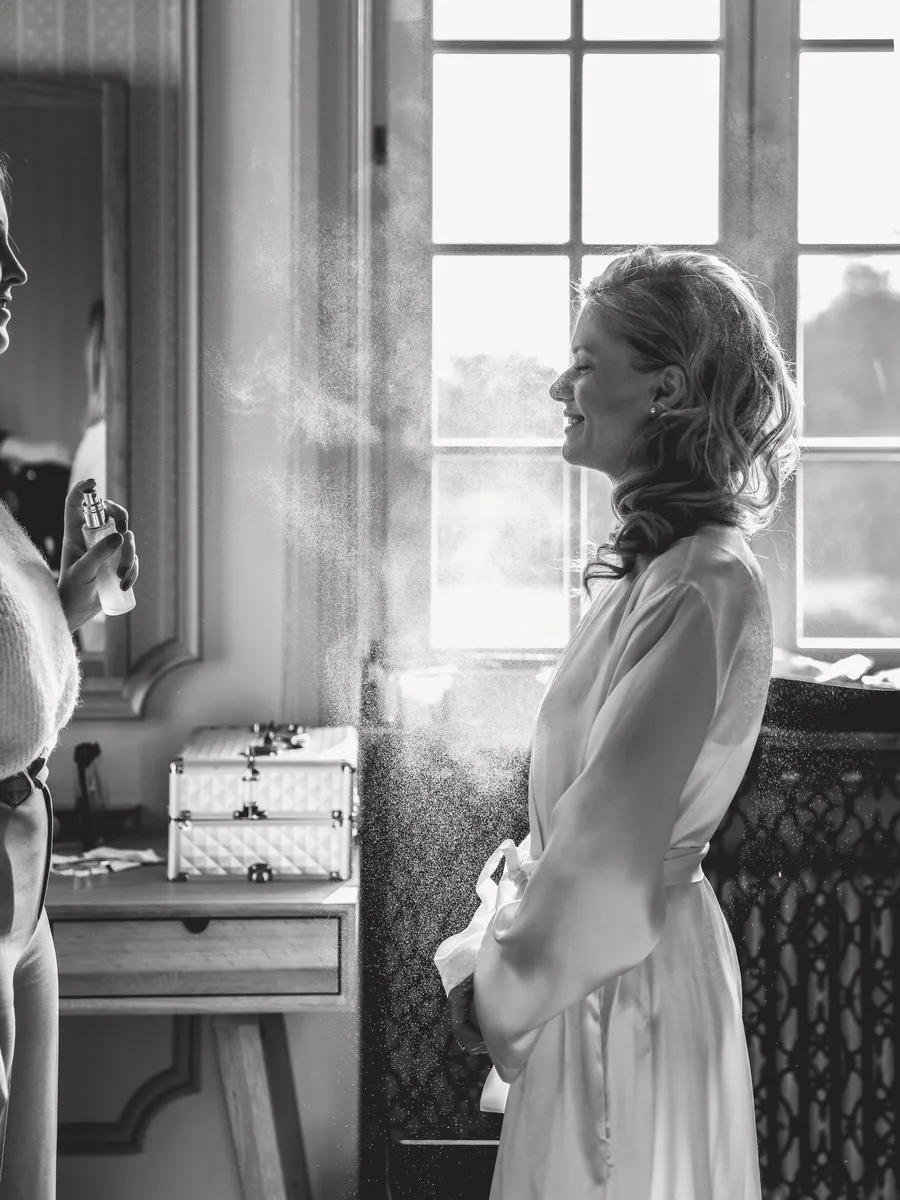 En noir et blanc, la mariée en peignoir regarde par la fenêtre.