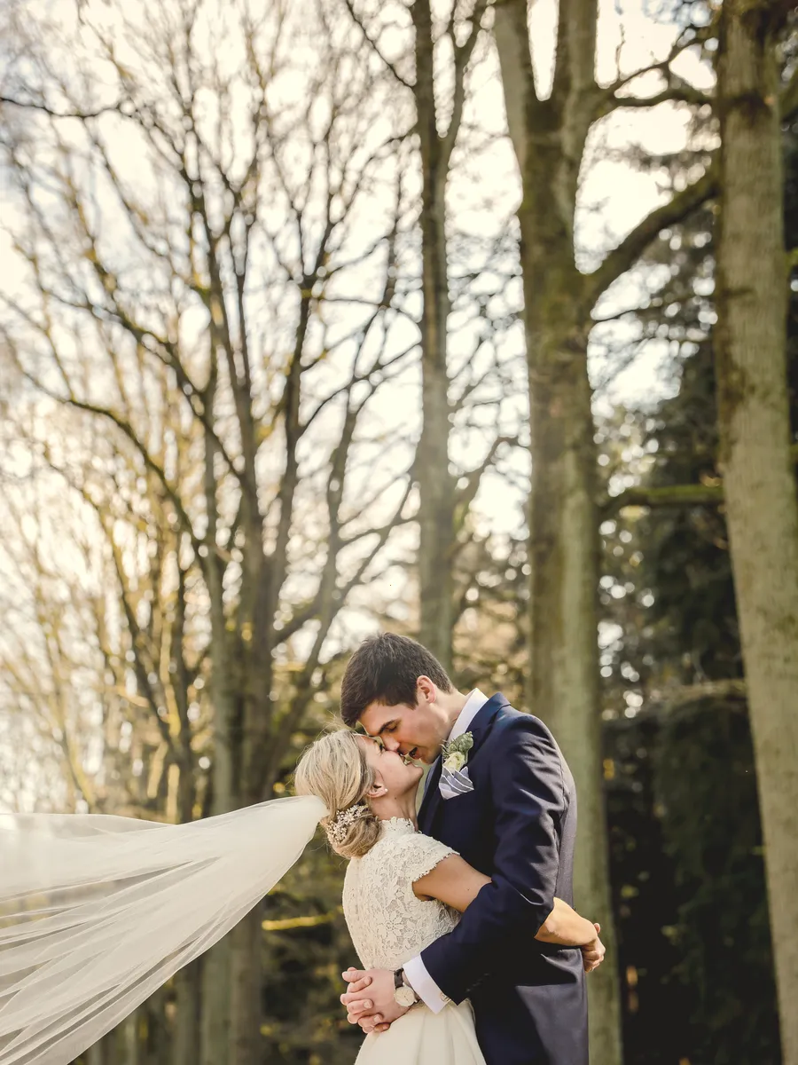 Le marié embrasse la mariée, le voile porté par le vent.