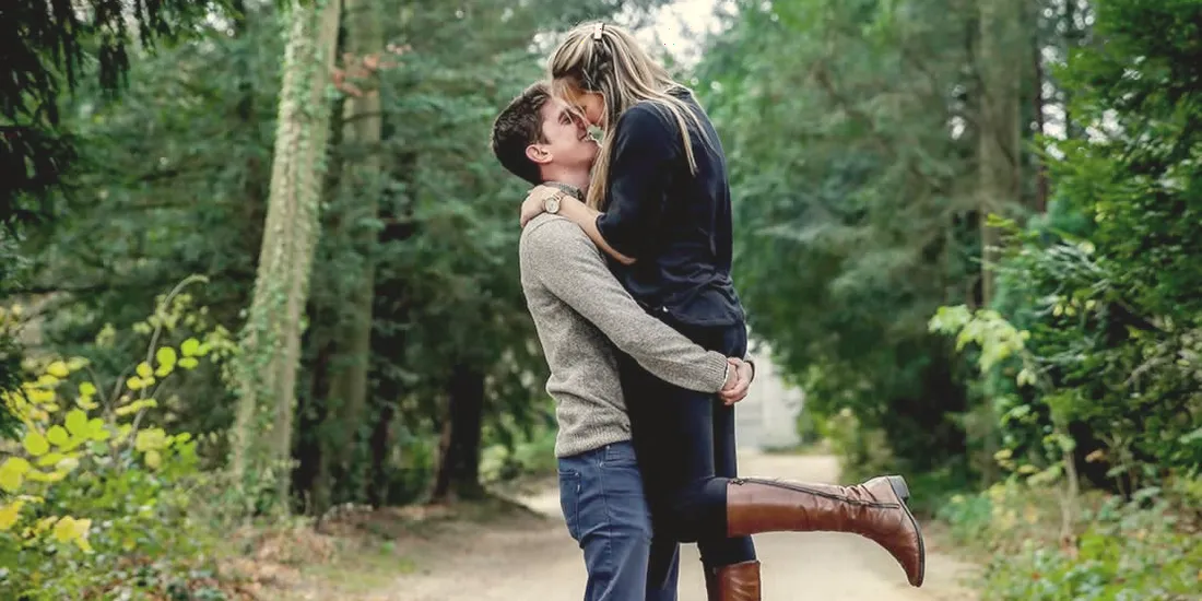 Séance engagement : le couple s’embrasse au milieu d’un chemin forestier.